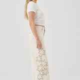 Woman wearing a white t-shirt and cream pants with star patterns on a plain background