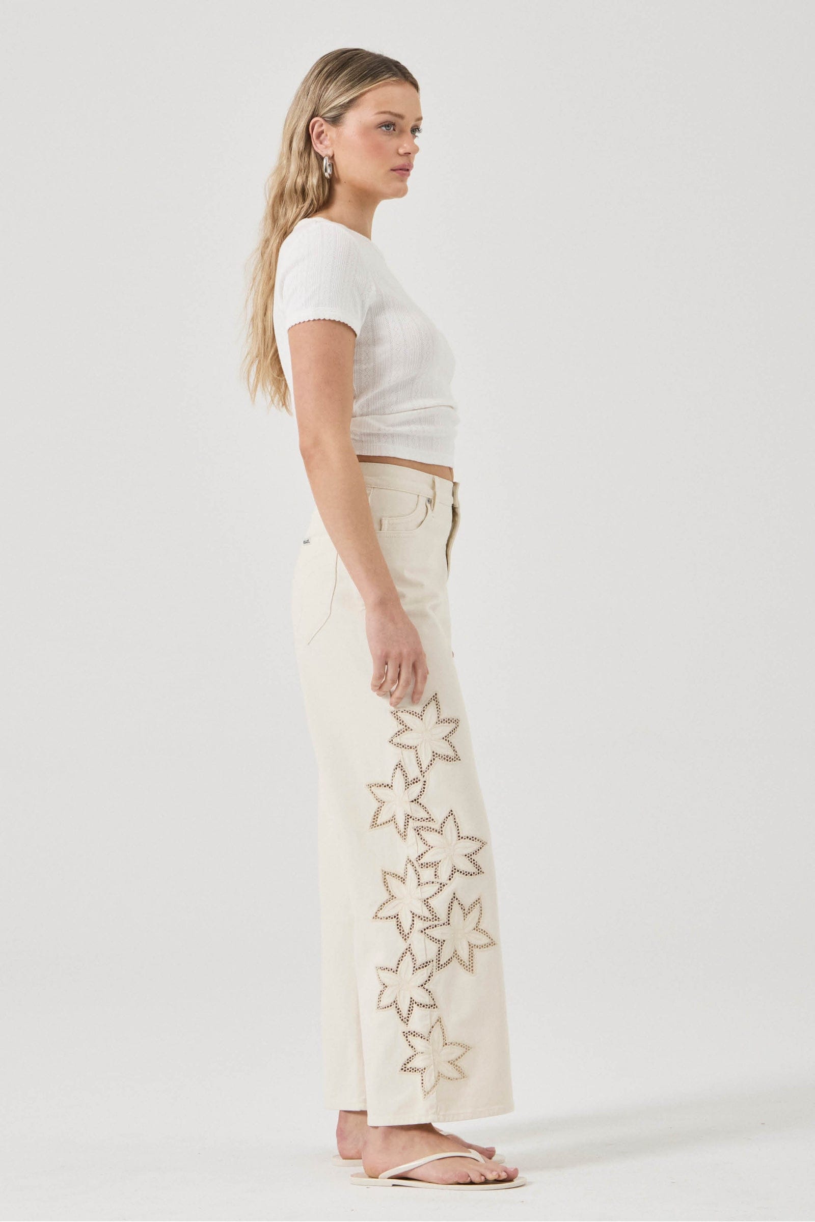 Woman wearing a white t-shirt and cream pants with star patterns on a plain background