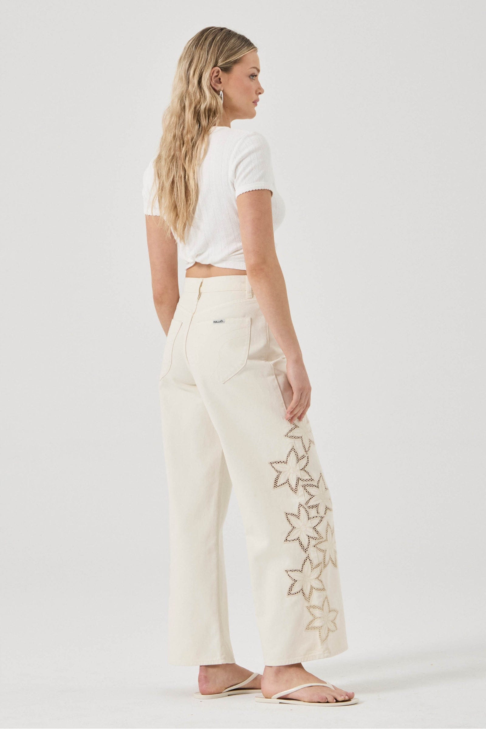 Woman wearing white pants with floral embroidery on a plain background