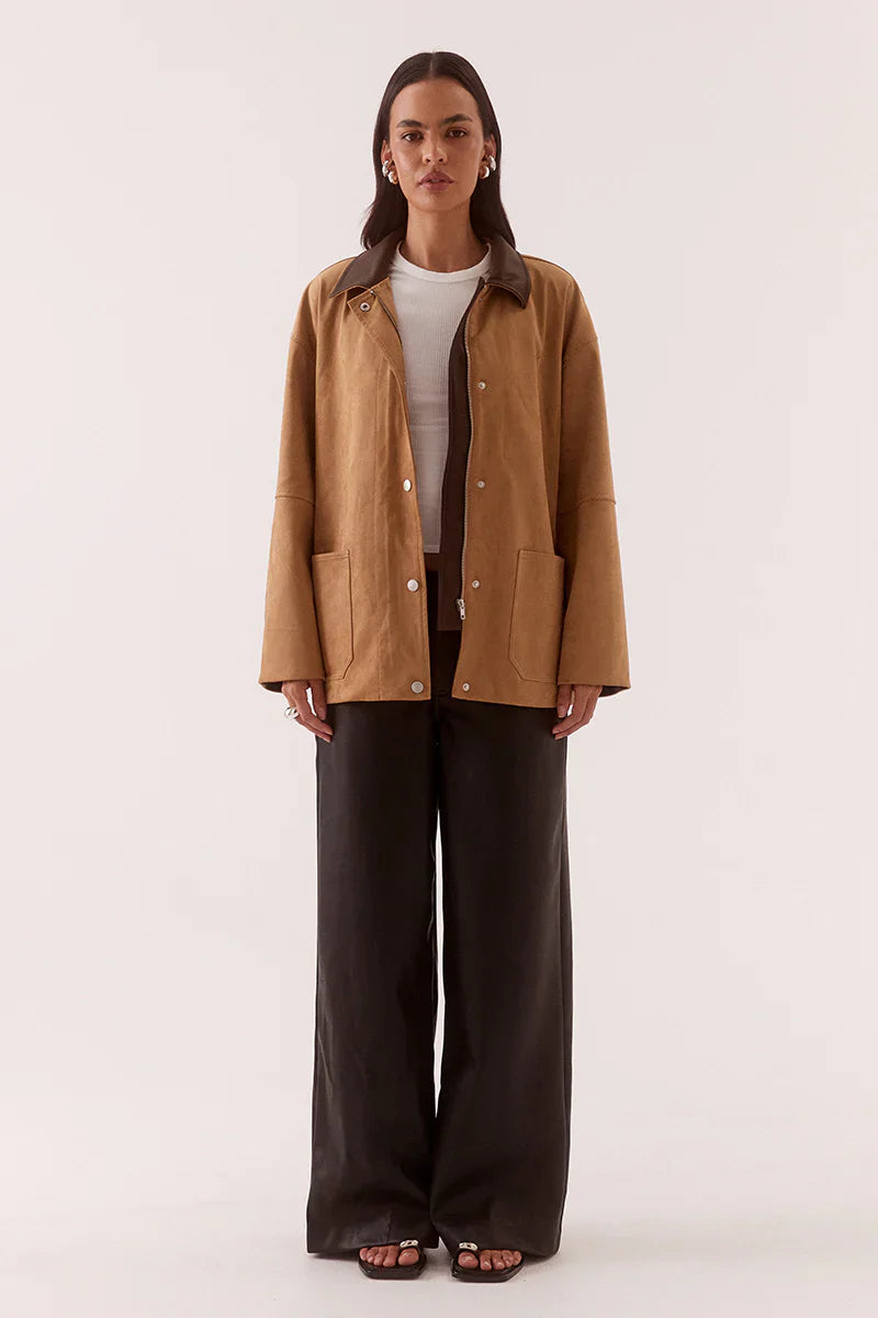 Woman wearing a brown jacket and dark pants on a white background