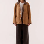 Woman wearing a brown jacket and dark pants on a white background
