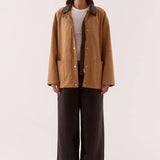 Woman wearing a brown jacket and dark pants on a white background