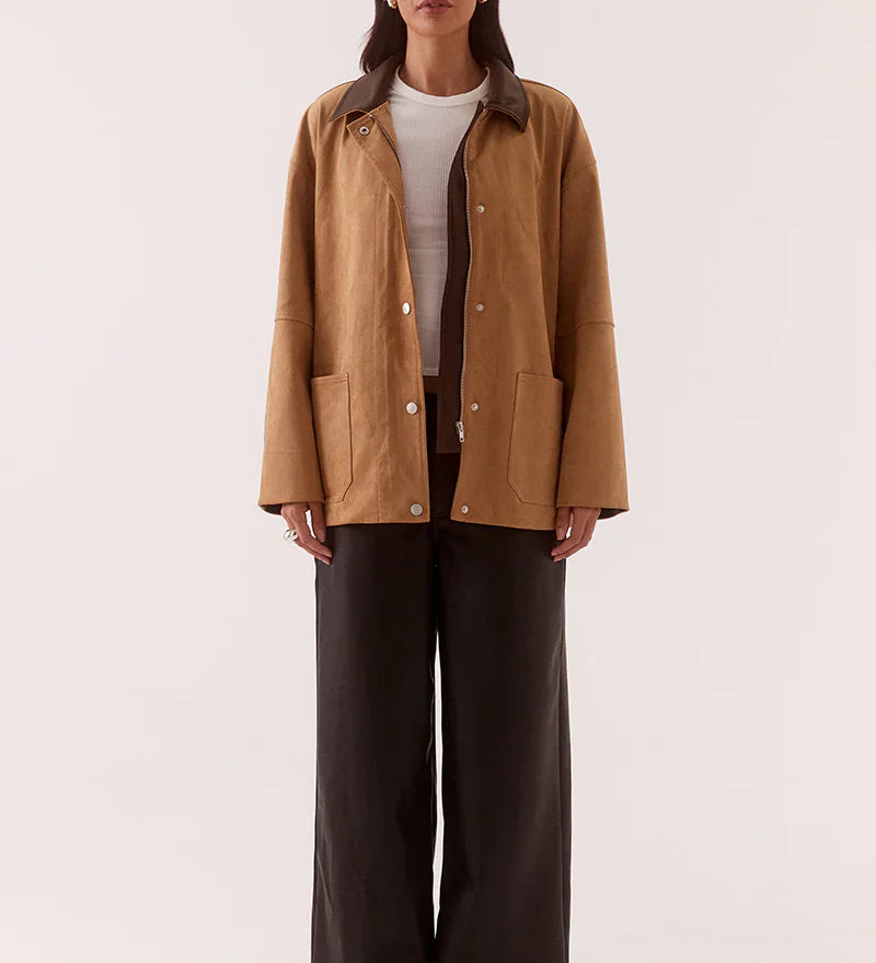 Woman wearing a brown jacket and dark pants on a white background
