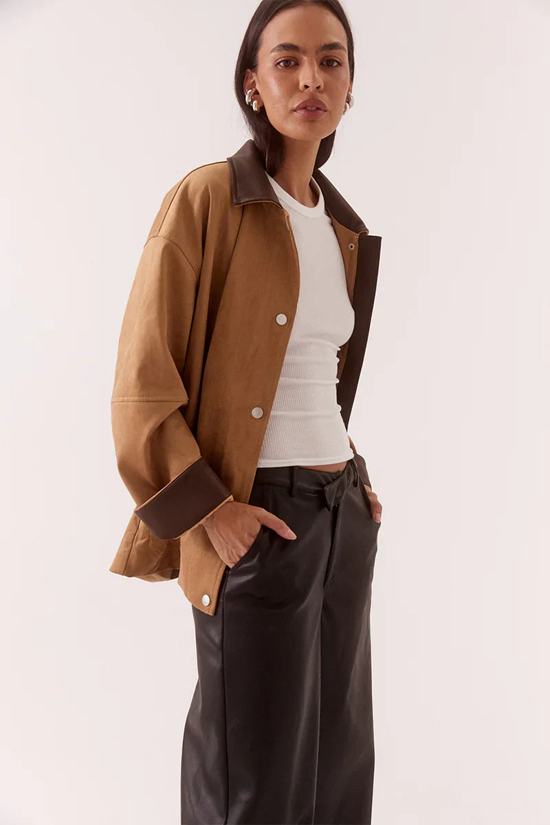 Woman wearing a brown jacket and dark pants on a white background