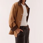 Woman wearing a brown jacket and dark pants on a white background