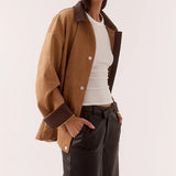 Woman wearing a brown jacket and dark pants on a white background