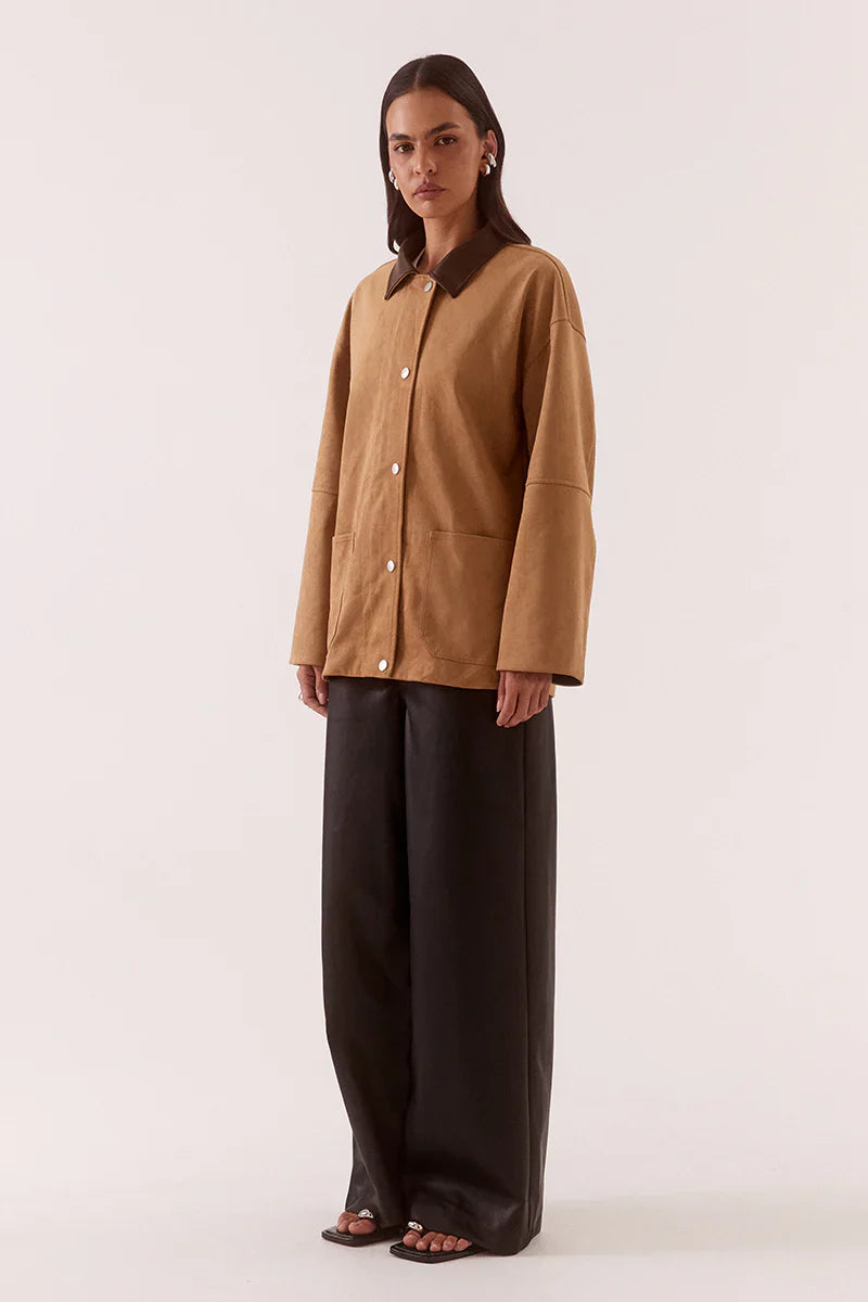 Woman wearing a brown jacket and black pants on a white background