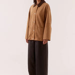 Woman wearing a brown jacket and black pants on a white background
