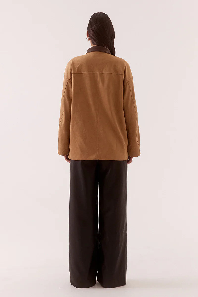 Person wearing a brown jacket and dark pants on a white background