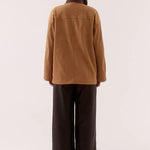 Person wearing a brown jacket and dark pants on a white background