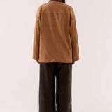 Person wearing a brown jacket and dark pants on a white background